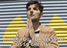 a man in a suit and bow tie is praying with his hands folded in front of a wall .