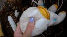 a person with purple nail polish holds a stuffed animal in their hand