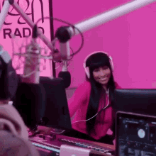 a woman wearing headphones is sitting in front of a microphone in front of a pink wall that says radio