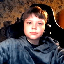 a young boy is sitting in a chair wearing headphones and a hoodie .