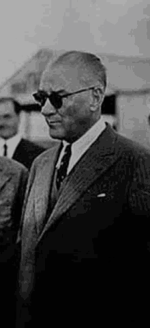 a man in a suit and tie is wearing sunglasses and standing next to another man .