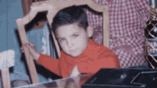 a young boy in an orange sweater sits in a chair with a bottle of pan ferrero in the background