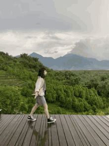 a woman is walking on a wooden deck overlooking a lush green forest