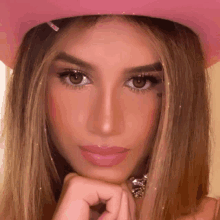 a woman wearing a pink cowboy hat and a necklace is looking at the camera .