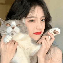 a young woman is holding a gray and white cat in her arms .