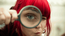 a woman with red hair is looking through a magnifying glass at her eye