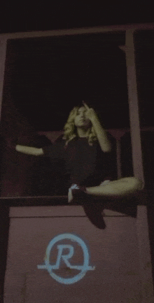 a woman is sitting on the side of a building with her legs crossed and smoking a cigarette at night .