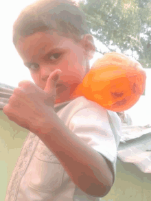 a young boy is holding an orange balloon and giving a thumbs up sign