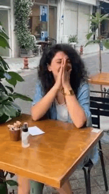 a woman is sitting at a table with her hands on her face and covering her face .