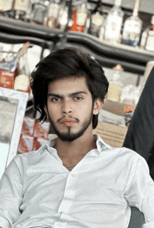 a young man in a white shirt stands in front of a shelf full of bottles including jack daniels