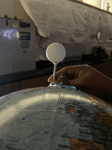 a person is holding a small white object on top of a globe in a dark room