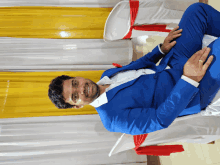 a man in a blue suit is sitting in front of a yellow curtain