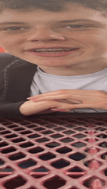 a young boy with braces on his teeth sits at a red picnic table