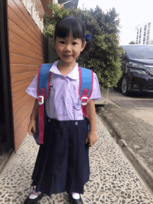 a little girl wearing a school uniform with a blue and pink backpack