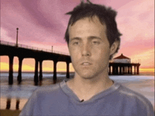 a man in a blue shirt stands in front of a pier at sunset