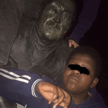 a boy laying next to a statue of a man with his eyes covered