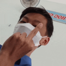 a man wearing a mask shows his middle finger in front of a sign that says học g