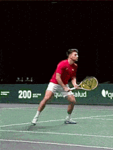 a man in a red shirt is holding a tennis racquet on a tennis court with a sign that says 200