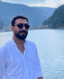 a man in a white shirt and sunglasses is standing in front of a body of water .