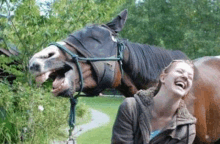 a woman is laughing next to a horse with its mouth open and a bridle on .