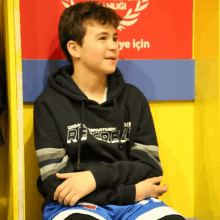 a boy wearing a black hoodie that says ' re real ' on it sits in a locker room