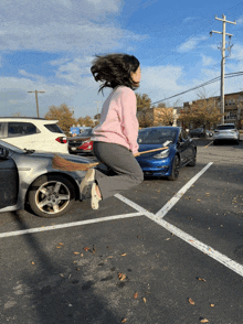 a woman in a pink sweater is jumping in the air on a broom in a parking lot