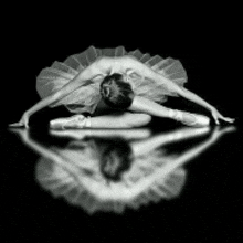 a black and white photo of a ballerina in a tutu and pointe shoes doing a split .