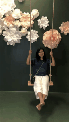 a woman is sitting on a swing in front of a wall of paper flowers