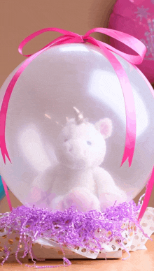 a stuffed unicorn is inside of a balloon with a pink bow