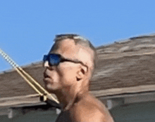 a shirtless man wearing sunglasses is standing next to a rope on a roof .