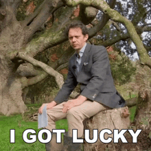 a man in a suit sits on a tree stump with the words " i got lucky " above him