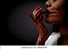 a woman with blood on her face and hands is holding her finger to her mouth .