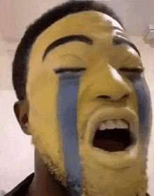 a man with a yellow face painted on his face is crying with tears running down his face .