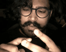 a man with glasses and a beard is holding his finger to his mouth