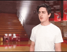 a man in a white shirt is standing in a gym with a basketball hoop in the background .