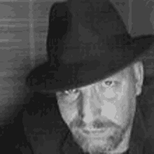 a man with a beard is wearing a hat and looking at the camera in a black and white photo .