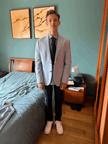 a young man wearing a suit and tie stands in front of a bed