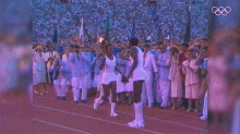 a man holding a torch stands in front of a crowd of people with the olympic rings in the background