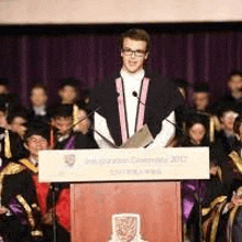 a man is standing at a podium giving a speech to a crowd of graduates .