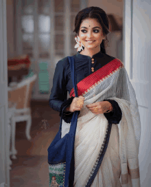 a woman wearing a black blouse and a white saree with a blue bag