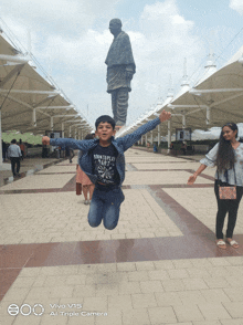 a boy is jumping in the air in front of a statue with a vivo v15 at the bottom