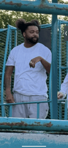 a man in a white shirt is standing in front of a blue metal fence