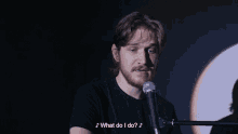 a man singing into a microphone with the words " what do i do " above him