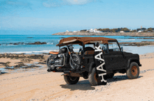 a black jeep is parked on the beach with a motorcycle and a surfboard on the back