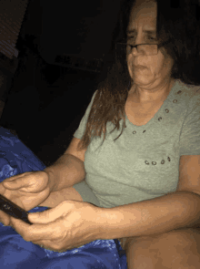 a woman wearing glasses is sitting on a bed looking at her cell phone