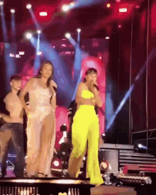 a woman in a yellow jumpsuit singing into a microphone on stage