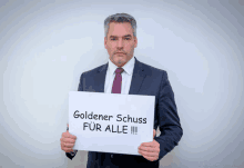 a man in a suit holds up a sign that says goldener schuss for alle