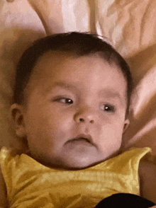 a baby in a yellow shirt is laying on a bed and looking at the camera