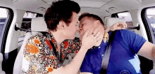 two men are kissing in a car and one of them is holding the other 's face .