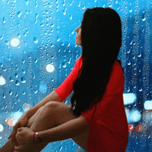 a woman in a red dress sitting in front of a window with rain drops on it